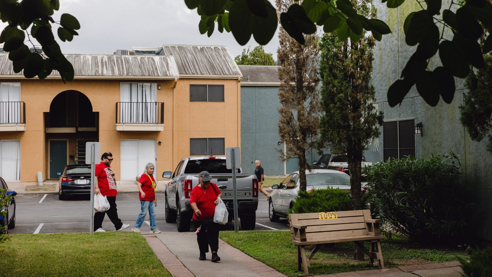 A group of ​people walk on‍ a sidewalk in front of a two story apartment building