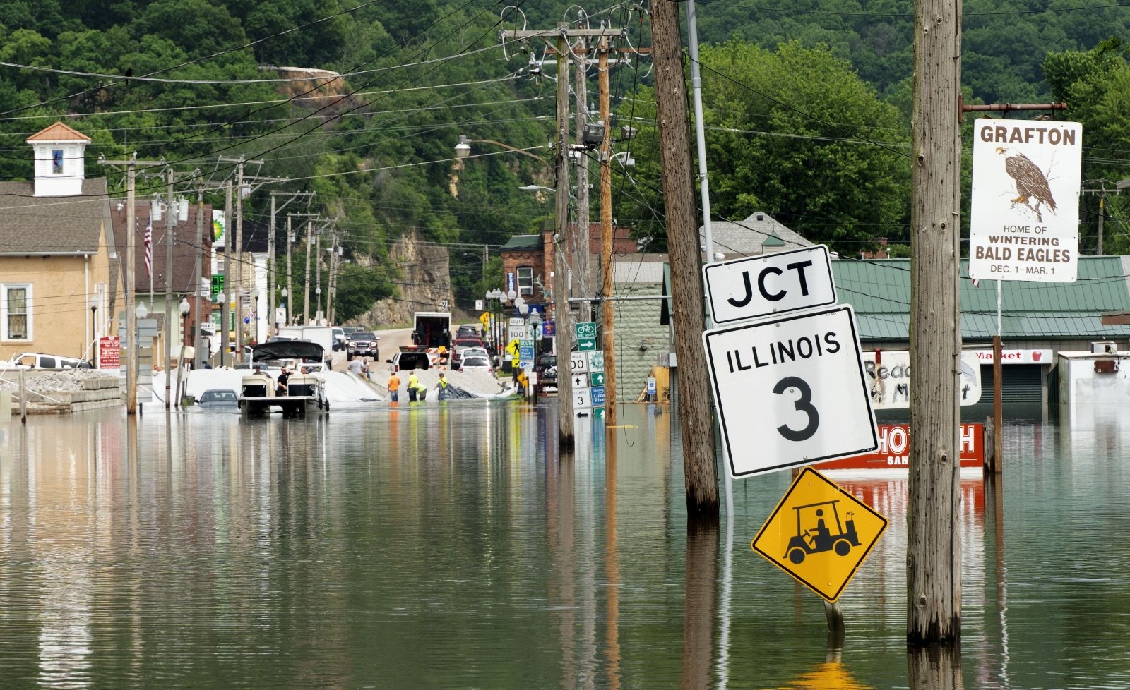 A sign that says Illinois 3 jct on a small town street is surrounded by‌ flood waters